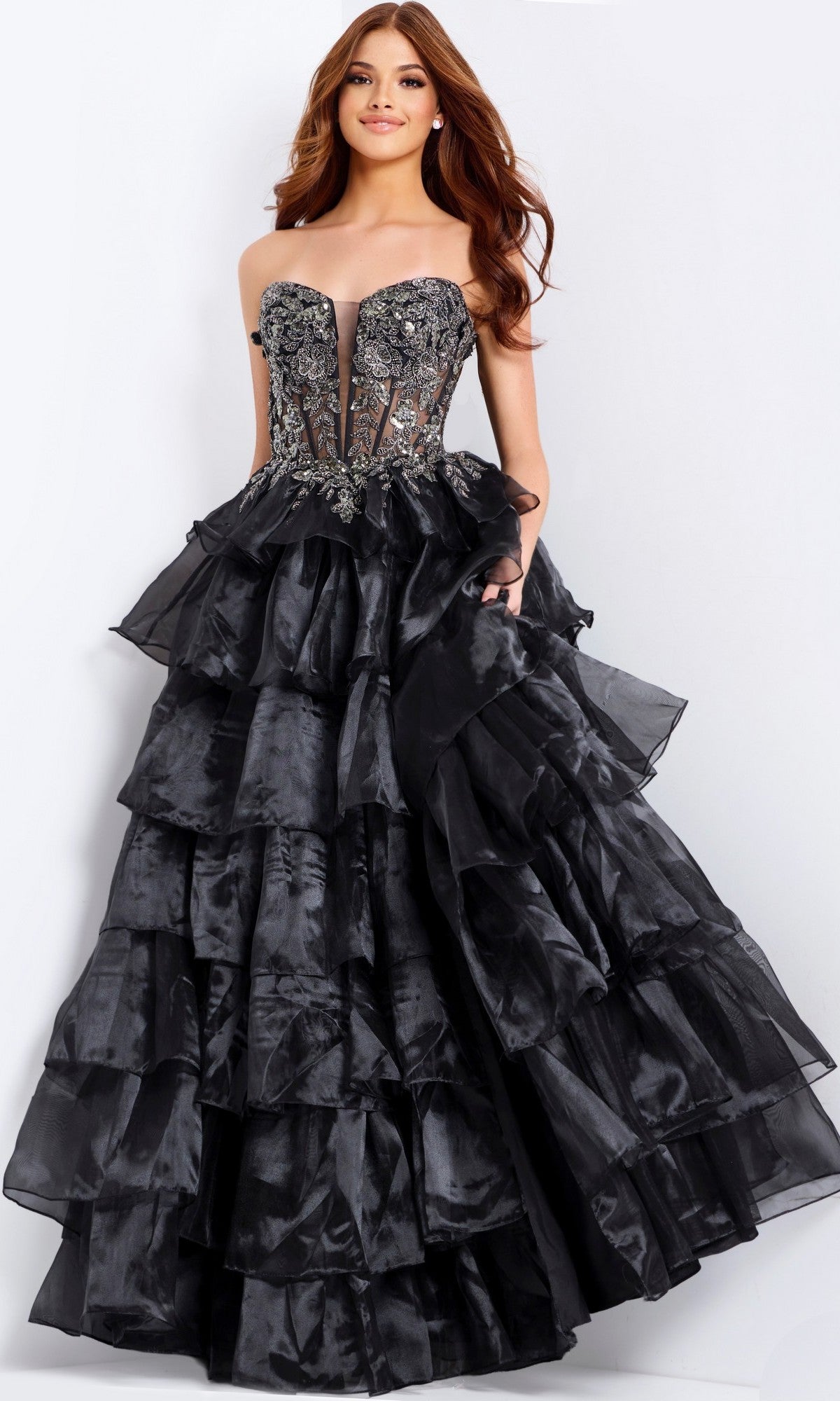 A woman wears the Jovani 50259 long prom dress—a strapless black gown with a tiered ruffle skirt and embroidered corset bodice—standing against a plain background.
